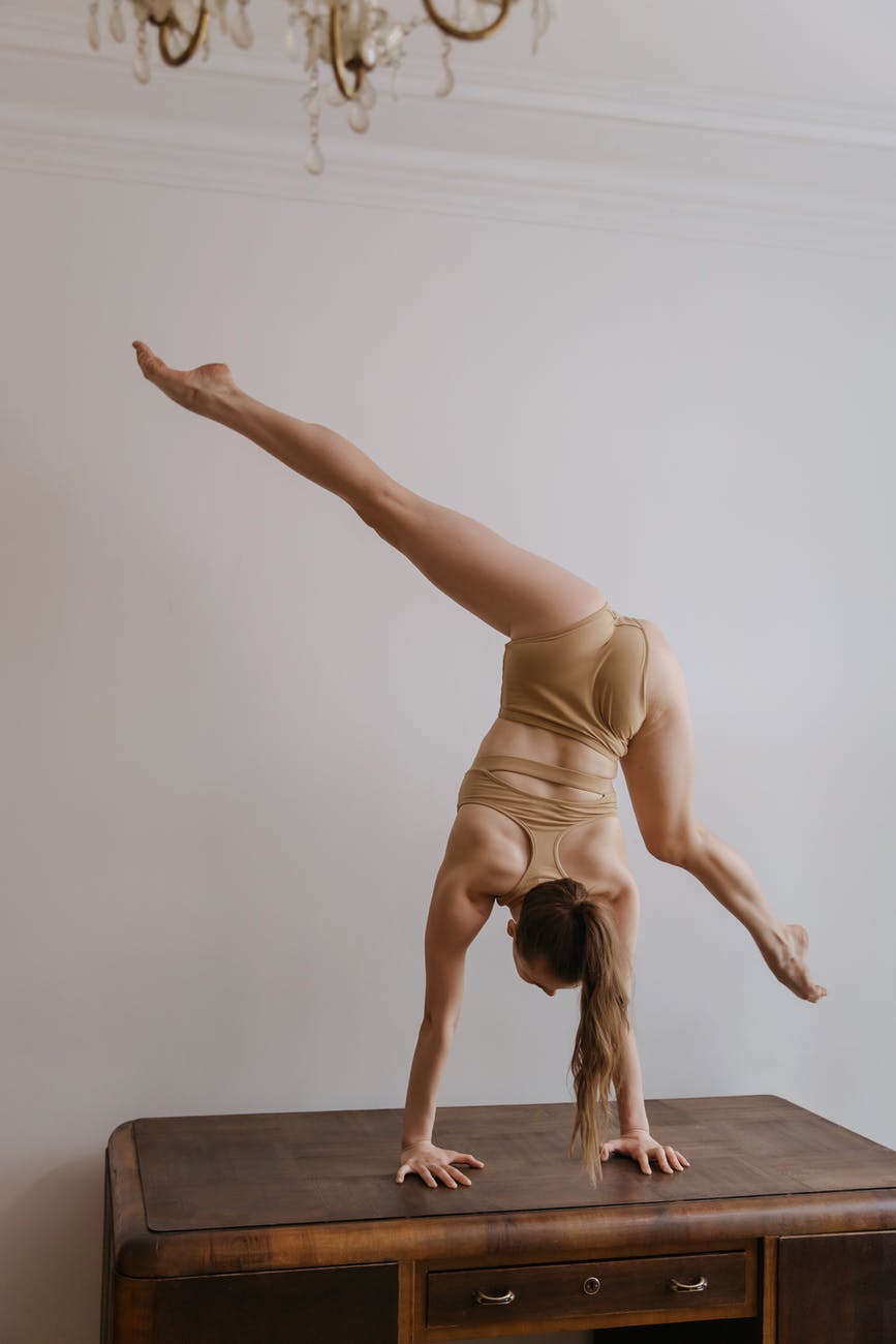 a woman doing a hand stand splits on a wooden desk